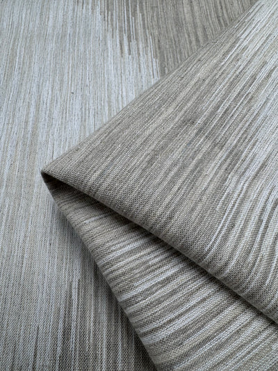 The Linen Blend - Solana fabric by Super Cheap Fabrics features a close-up of folded beige material with a subtle, textured pattern of vertical lines in varying shades of beige and light gray. The medium-weight material appears soft, exuding natural elegance. Width: 145cm.