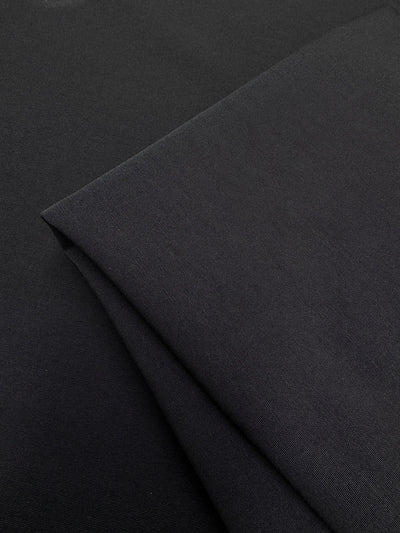 Close-up of Super Cheap Fabrics' Stretch Bengaline - Moonless Night (150cm), a medium weight black fabric with a smooth, slightly textured surface, shown folded on top of stretch woven material.