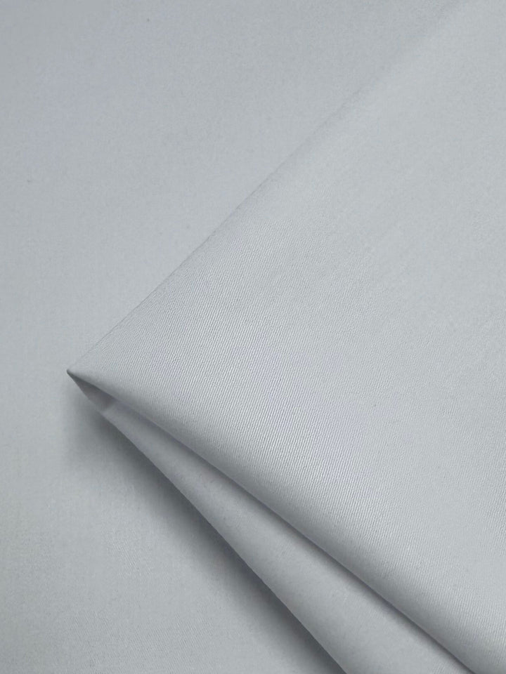 A neatly folded piece of white gabardine fabric from Super Cheap Fabrics, measuring 150cm, lies on a flat surface with its smooth and wrinkle-resistant texture featuring subtle diagonal lines.