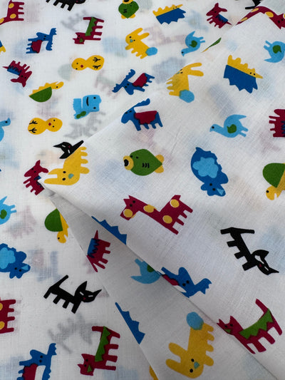 Close-up of Super Cheap Fabrics' Printed Poplin - 112cm, a lightweight non-stretch poly-cotton fabric with playful red, yellow, blue, green, and black animal illustrations on a white background. It features stylized cats, birds, and turtles scattered across the design.