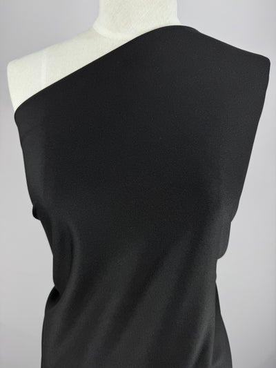 Textured Knit - Ripple - 155cm by Super Cheap Fabrics, a medium-weight black polyester fabric drapes elegantly over a mannequin's shoulder against a light gray backdrop, highlighting its asymmetrical style.