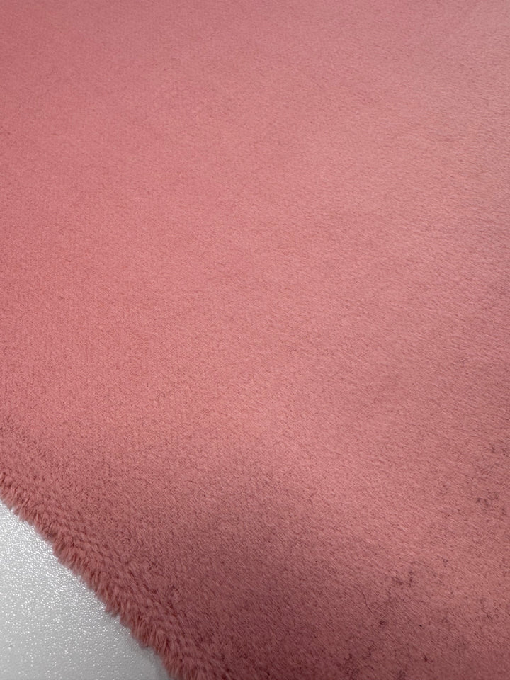The Wool Cashmere - Coral Almond fabric by Super Cheap Fabrics showcases luxurious softness with its textured pink surface. The slightly fluffy texture with visible fibers and shade variations captures the material's depth from an angled perspective, reminiscent of plush fur.