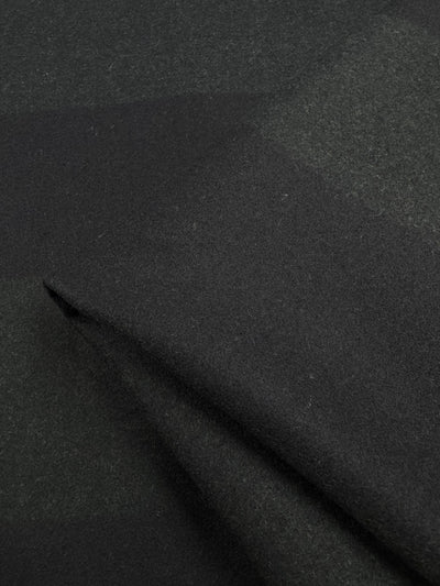 Close-up of Super Cheap Fabrics' Virgin Wool in a two-tone black khaki pattern. The soft, heavy weight wool displays a subtle plaid design, with gentle folds emphasizing its texture and weave. Width: 150cm.