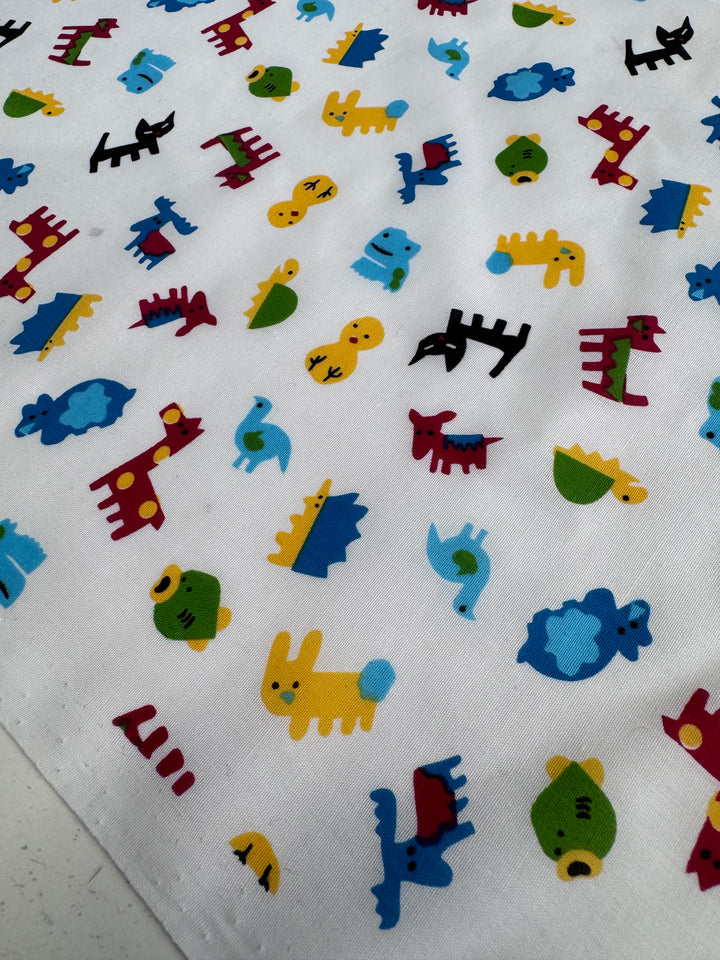 The Printed Poplin by Super Cheap Fabrics is a lightweight poly-cotton fabric featuring colorful animal designs like horses, ducks, camels, sheep, and dinosaurs in vibrant reds, yellows, blues, greens, and blacks scattered on the non-stretch 112cm wide fabric.