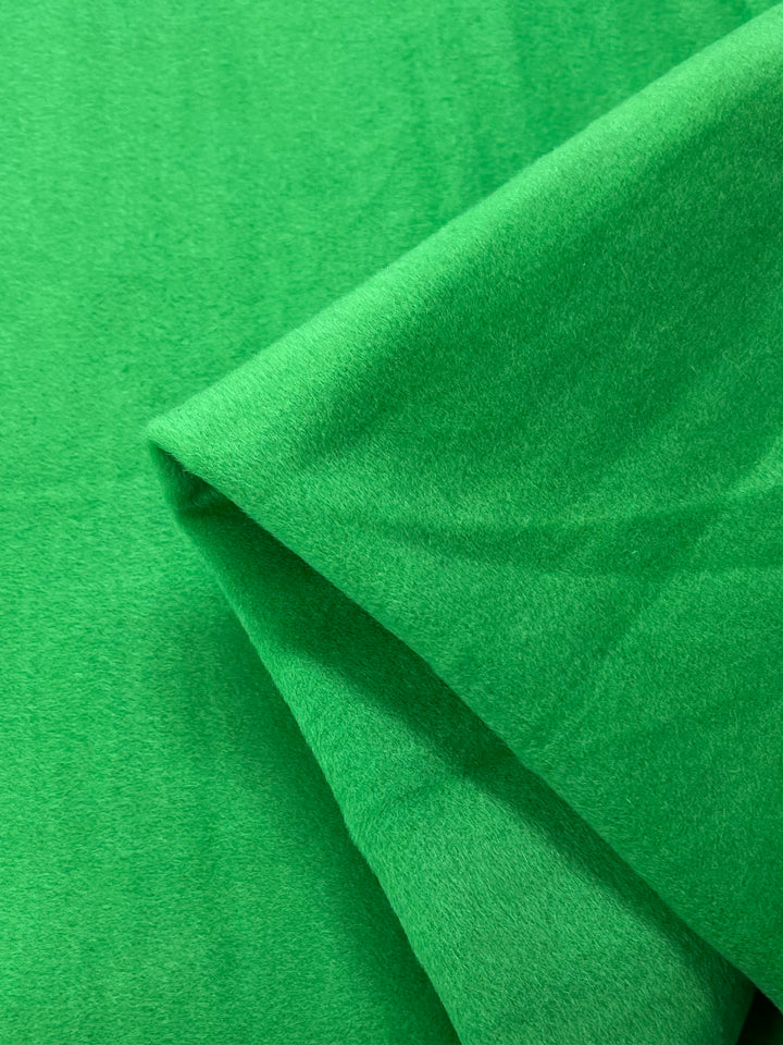 Close-up of the Titanite Wool Cashmere fabric by Super Cheap Fabrics. This vibrant green material, 150cm wide, showcases its plush texture and flexibility through soft folds, smooth lines, and subtle shadows.