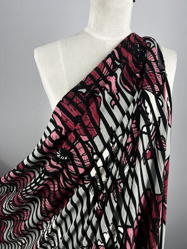 The Textured Lycra - Poppy Dream from Super Cheap Fabrics elegantly drapes over a mannequin's shoulder. This 150cm fabric features bold black and white stripes with maroon and black abstract designs, creating a striking yet sophisticated look.