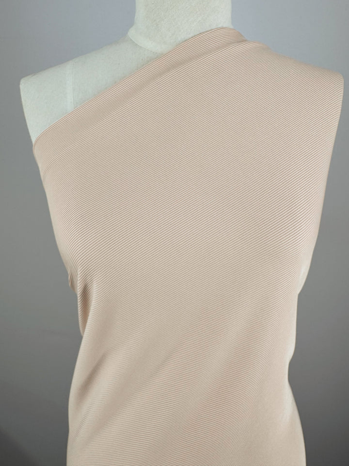 The mannequin features Super Cheap Fabrics' "Rib Knit - Biscuit - 130cm," an off-the-shoulder top in light beige with thin horizontal stripes. Crafted from medium-weight rib knit fabric, it drapes elegantly, offers generous stretch, and showcases minimalist style against a plain gray background.