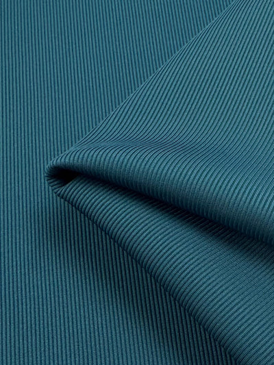 The close-up of folded teal fabric reveals the ribbed texture of Super Cheap Fabrics' Rib Knit 1x1 - Teal - 125cm, with a neat edge creating subtle shadows and showcasing detailed parallel ridges.