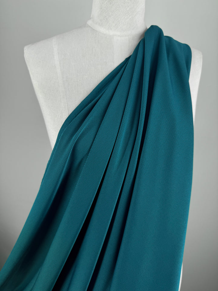 A mannequin draped with Super Cheap Fabrics' Rib Knit 1x1 in teal, 125cm wide, arranged over one shoulder against a plain gray background.