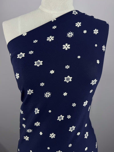 A torso mannequin displays the Super Cheap Fabrics' Printed Cotton Lycra - Twinkle, featuring dark blue fabric with white stars and floral motifs. The luxurious item measures 160cm. A plain, light gray backdrop highlights its elegance.