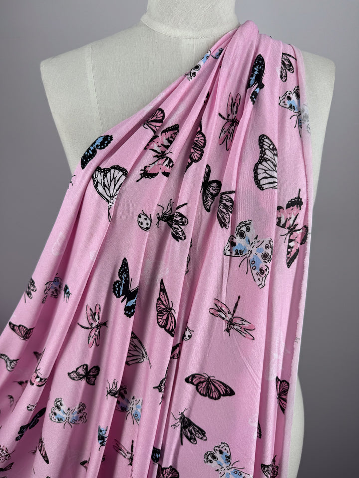 A mannequin is draped in Printed Cotton Lycra - Pink Fly from Super Cheap Fabrics, showcasing a vibrant butterfly pattern in black, white, blue, and pink.