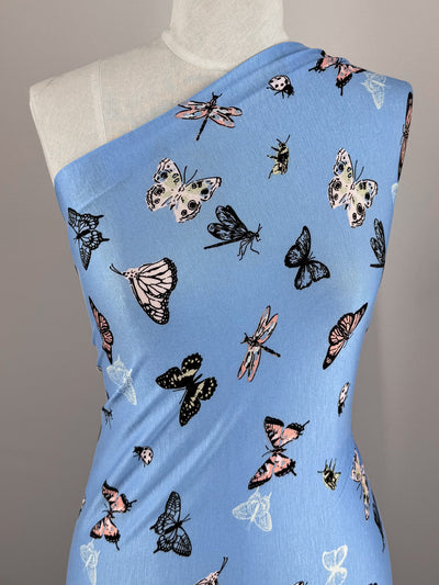 The Printed Cotton Lycra - Blue Butter - 155cm by Super Cheap Fabrics features a one-shoulder design with insects in pink, black, and white dancing across the cotton spandex fabric.