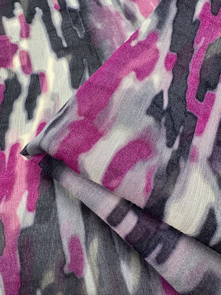 Close-up of folded Electric Mirage Pure Silk by Super Cheap Fabrics, featuring an abstract pattern in magenta, black, gray, and white. The soft texture and watercolor-like colors exude elegance reminiscent of high-end fashion. Width: 132cm.