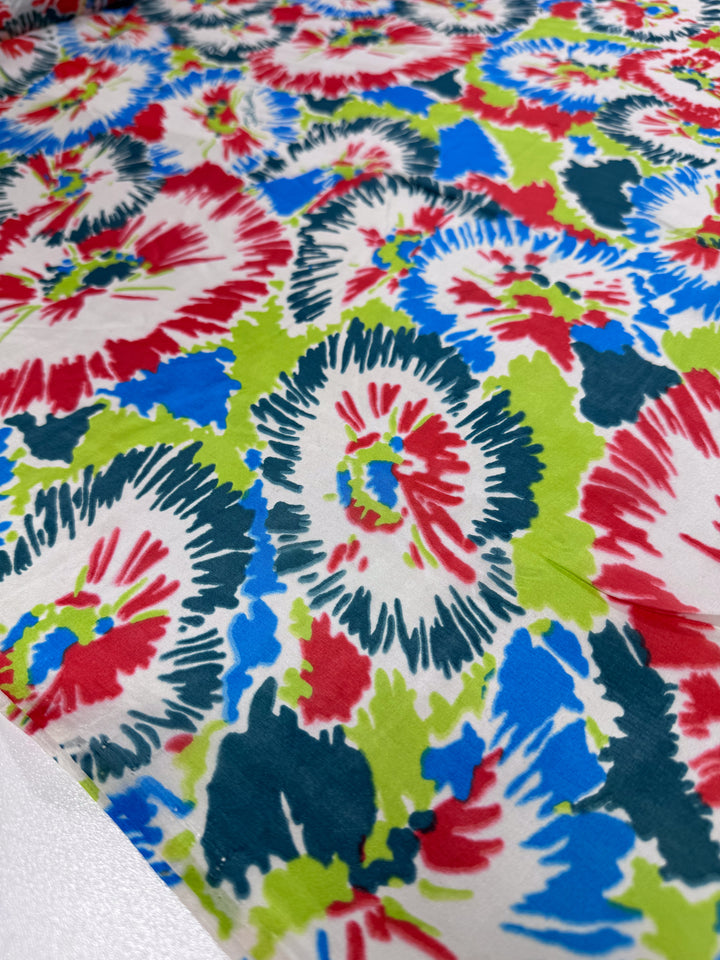 A close-up of vibrant florals and leaves in red, blue, green, and white on Super Cheap Fabrics' Pure Silk - Splash - 140cm showcases an energetic design perfect for luxury fashion.