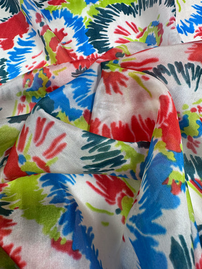 The Pure Silk - Splash - 140cm from Super Cheap Fabrics is a vibrant multicolored fabric with tie-dye splashes of red, blue, green, and black on white. It drapes artistically to create gentle folds and a textured effect for luxury fashion attire.