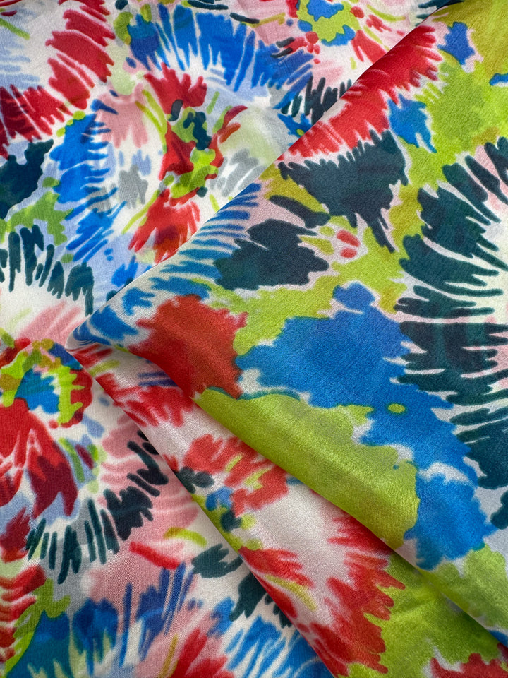 Pure Silk - Splash - 140cm by Super Cheap Fabrics features a luxurious, colorful tie-dye pattern with irregular red, blue, green, and black shapes on white. Made from pure printed silk, it exudes dynamic energy perfect for high-end fashion.
