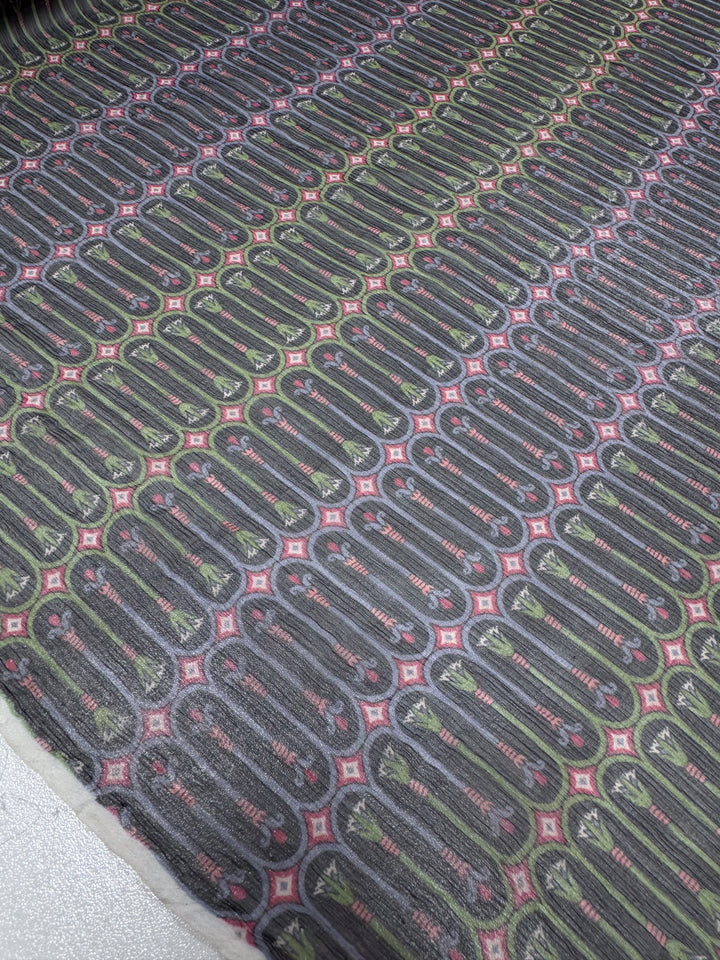A close-up of Pure Silk - Serpent Bloom - 135cm by Super Cheap Fabrics shows a luxury fabric with dark ovals and red squares on a pale background, forming a geometric grid pattern, ideal for high-end fashion attire.