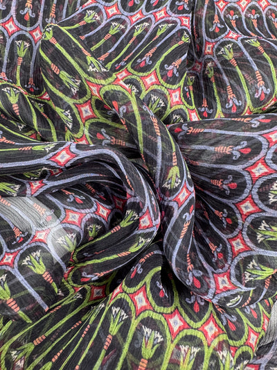 Close-up of a colorful fabric crafted from Pure Silk - Serpent Bloom - 135cm by Super Cheap Fabrics, featuring an intricate red, green, and black design. The luxurious material is slightly crumpled with floral and geometric shapes, perfect for high-end fashion attire.