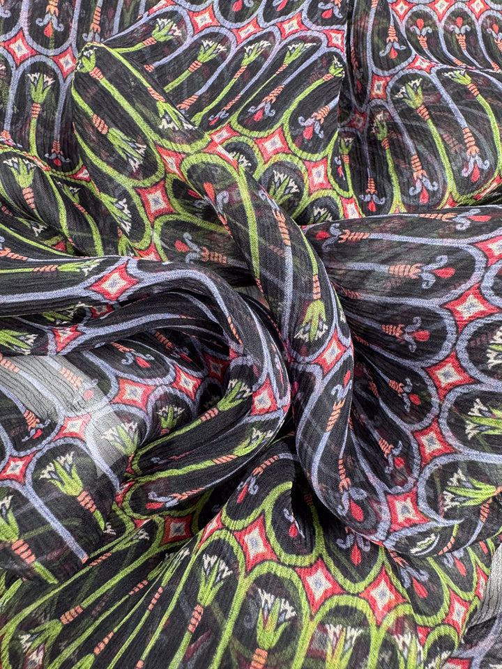 Close-up of a colorful fabric crafted from Pure Silk - Serpent Bloom - 135cm by Super Cheap Fabrics, featuring an intricate red, green, and black design. The luxurious material is slightly crumpled with floral and geometric shapes, perfect for high-end fashion attire.