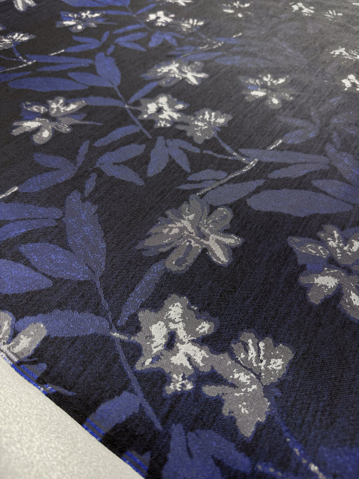 A close-up of the Designer Jacquard - Navy Rose fabric from Super Cheap Fabrics shows a dark polyester texture with intricate navy and white floral patterns, creating a rich and elegant appearance.