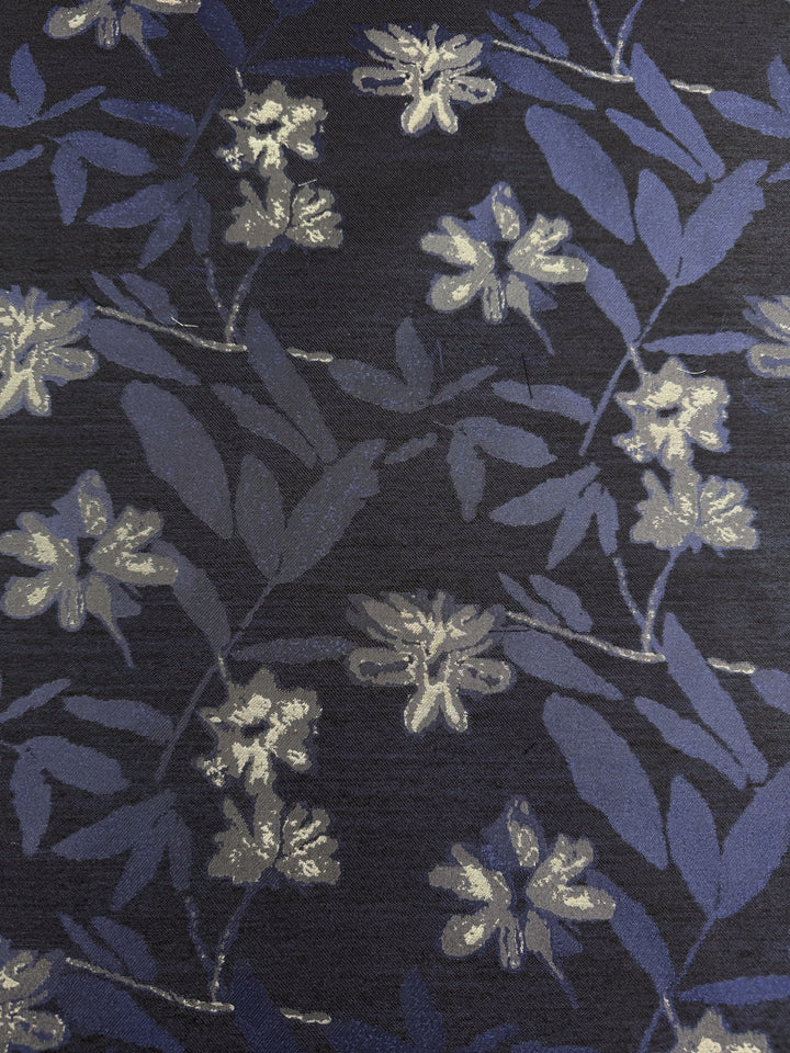 The Designer Jacquard - Navy Rose by Super Cheap Fabrics features an intricate floral pattern with white flowers and blue leaves on a dark navy background. Made from textured polyester, this elegant fabric measures 150cm wide.