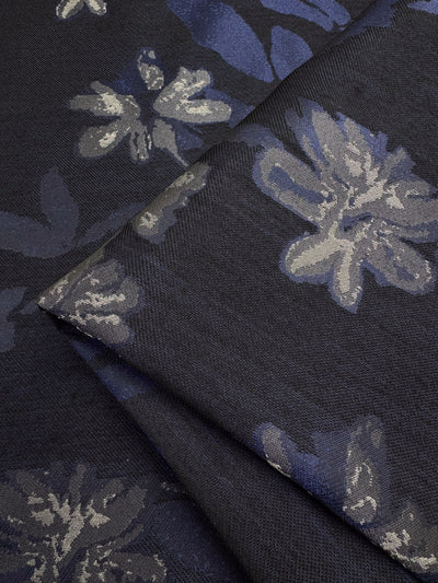 A close-up of the Designer Jacquard - Navy Rose by Super Cheap Fabrics shows a navy polyester fabric with intricate blue and gray floral patterns, artfully folded to display flowers and leaves across its 150cm width.
