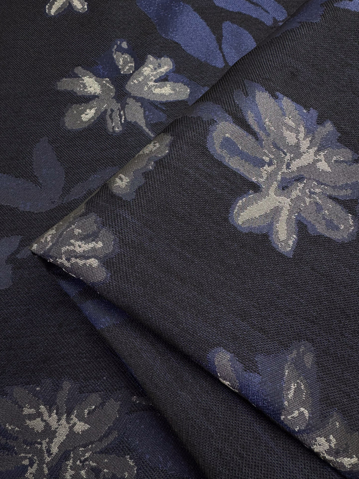 A close-up of the Designer Jacquard - Navy Rose by Super Cheap Fabrics shows a navy polyester fabric with intricate blue and gray floral patterns, artfully folded to display flowers and leaves across its 150cm width.