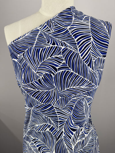 A mannequin is draped with Super Cheap Fabrics' Printed Lycra in Sapphire, featuring a bold blue and white abstract leaf design crafted from medium-weight Polyester/Spandex. Styled over one shoulder, it presents an elegant and modern look.