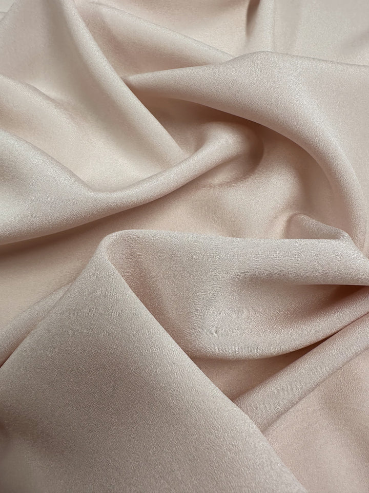 Close-up of Super Cheap Fabrics' Crepe - Mauve Chalk - 150cm, a soft polyester fabric with a smooth texture. It drapes in gentle folds, creating subtle shadows and highlights.