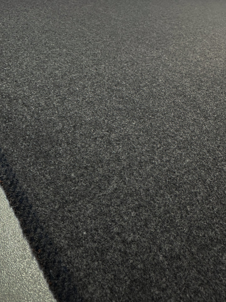 Close-up of Super Cheap Fabrics' Melton Wool in Charcoal Marle (150cm), showcasing a textured, dark gray surface with a soft, fuzzy feel. The carpet's edge is visible, providing a subtle contrast to the surrounding area.
