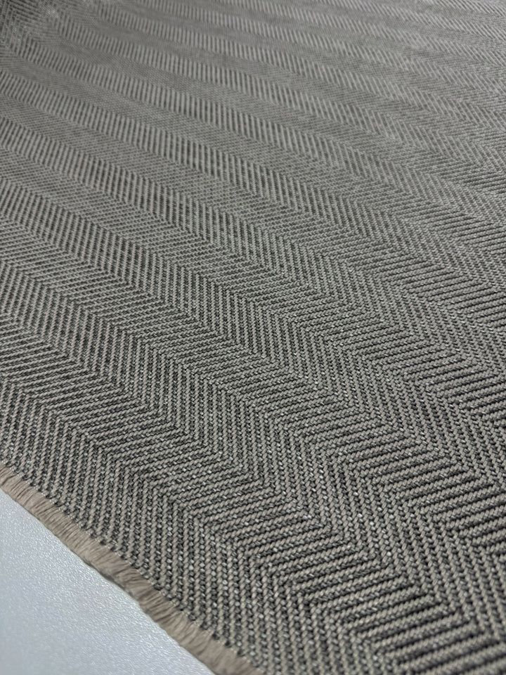 The Super Cheap Fabrics upholstery "Montpellier 26 - 145cm" features a gray herringbone pattern with a textured surface, ideal for high-traffic areas. The fabric lies flat, showcasing its intricate zigzag design and subtle sheen under light.