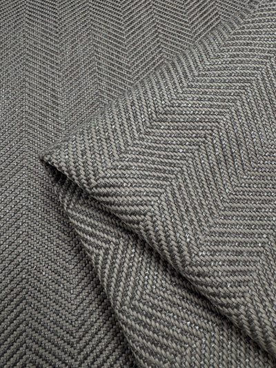 Close-up of Super Cheap Fabrics' Upholstery - Montpellier 26 - 145cm fabric highlights its gray herringbone pattern. The intricate weave, revealed in folds, offers a sophisticated and timeless look ideal for high-traffic areas.