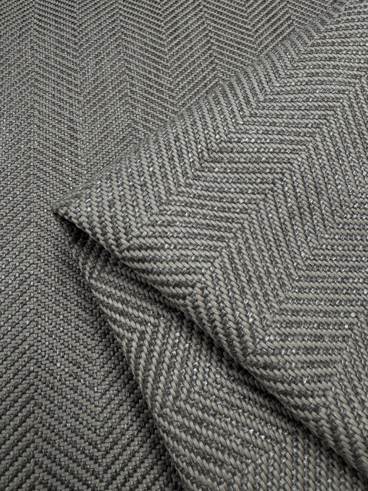Close-up of Super Cheap Fabrics' Upholstery - Montpellier 26 - 145cm fabric highlights its gray herringbone pattern. The intricate weave, revealed in folds, offers a sophisticated and timeless look ideal for high-traffic areas.