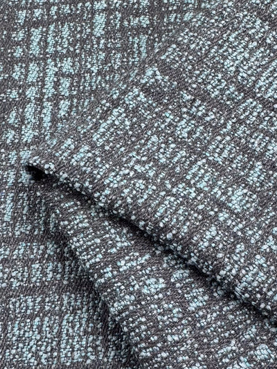 A close-up of Super Cheap Fabrics' Upholstery - Dexter 37 - 147cm shows a gray and light blue woven pattern, made from polyester and viscose. The fabric's folded thickness highlights a grid-like design with a speckled appearance.