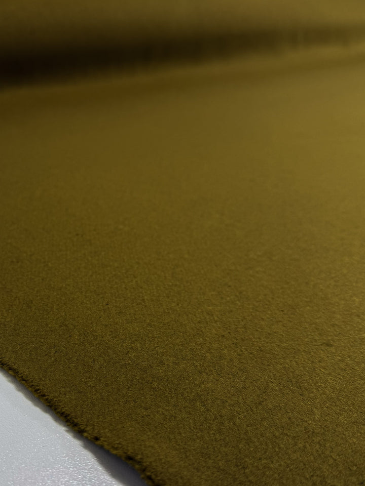 A close-up of Super Cheap Fabrics’ Wool Cashmere - Plantation (155cm) in olive green, a medium-heavy fabric with a soft, fuzzy texture, laid flat on white. The slightly uneven edge is visible in the foreground.