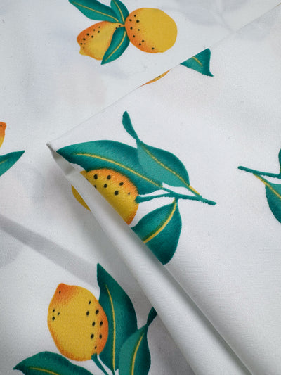 Close-up of Super Cheap Fabrics' Cotton Sateen - Lemon Grove (145cm), featuring a vibrant printed pattern of yellow lemons, green leaves, and brown stems on slightly folded cotton sateen fabric.