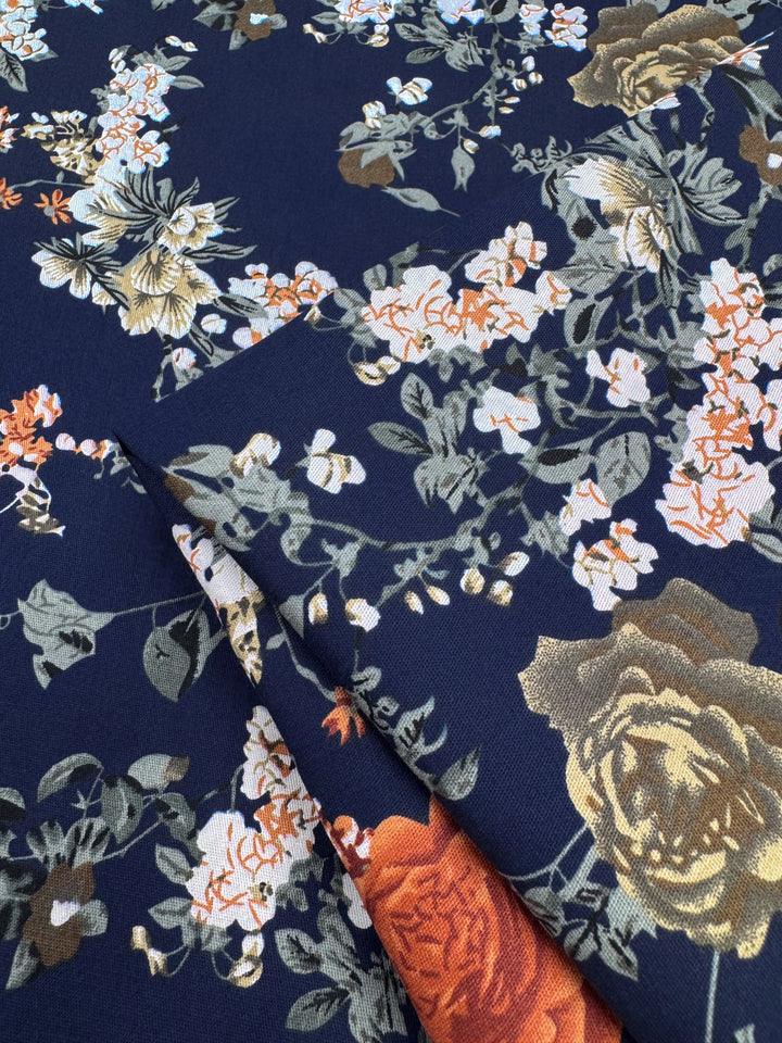 Super Cheap Fabrics' Cotton Sateen - Autumn Romance (145cm) features a lightweight navy blue fabric with white, orange, gold, and green floral patterns—ideal for cotton dresses and folded to showcase its vibrant design.