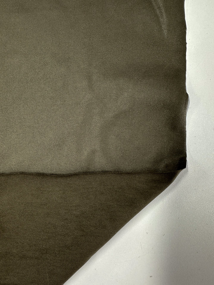 The Faux Spandex Leather - Tea Leaf by Super Cheap Fabrics is a textured, medium-weight fabric laid flat on a white surface, featuring a visible seam horizontally across the middle. The high-end material forms shadows and subtle folds, enhancing depth and appearance.
