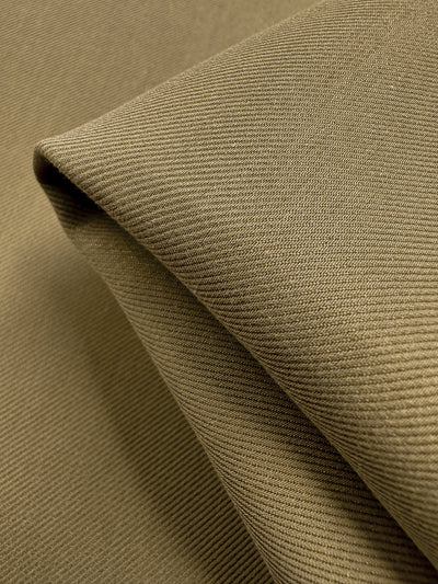 Close-up of neatly folded Designer Suiting - Incense - 140cm by Super Cheap Fabrics, showcasing visible diagonal weaves for a textured look. Arranged in sharp angles and soft shadows, this olive-green fabric is perfect for crafting elegant skirts, jackets, or coats with its smooth surface and subtle sheen.