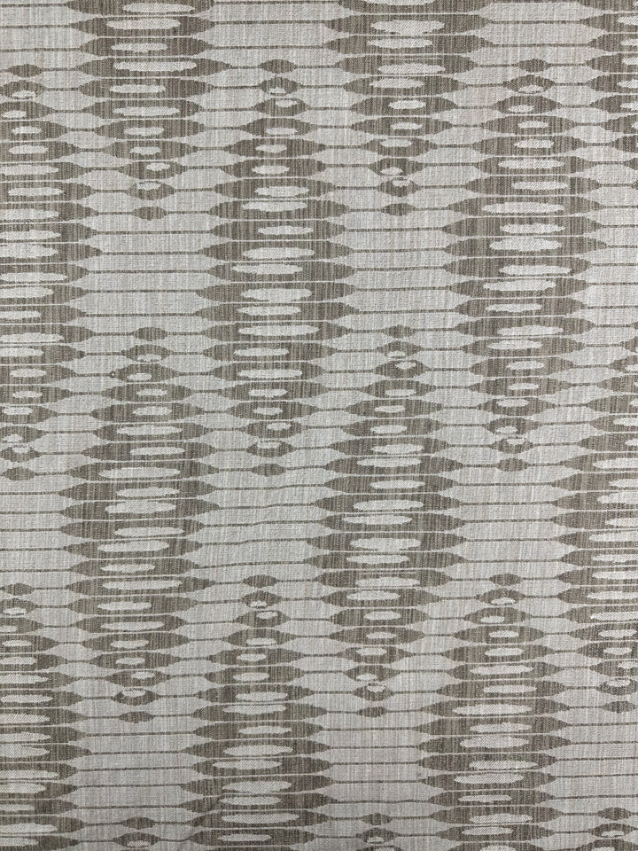 The Upholstery Jacquard - Ludwig Silver by Super Cheap Fabrics features an ikat-inspired abstract geometric pattern with a textured, woven look. It showcases symmetrical ovals and diamonds in gray and beige, reminiscent of luxurious upholstery fabric. Width: 140cm.
