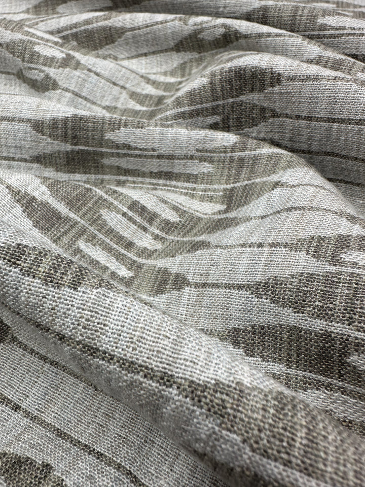 Close-up of the Ludwig Silver upholstery jacquard by Super Cheap Fabrics, showcasing ikat-inspired wavy stripes in gray and cream. The jacquard weave enhances depth, creating dynamic shadows and highlights across its beautifully draping 140cm fabric.