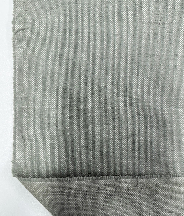 Close-up of Super Cheap Fabrics' Upholstery - Warm Silver - 142cm in a plain weave, showcasing thread details on a smooth white surface, with one corner folded to reveal texture.