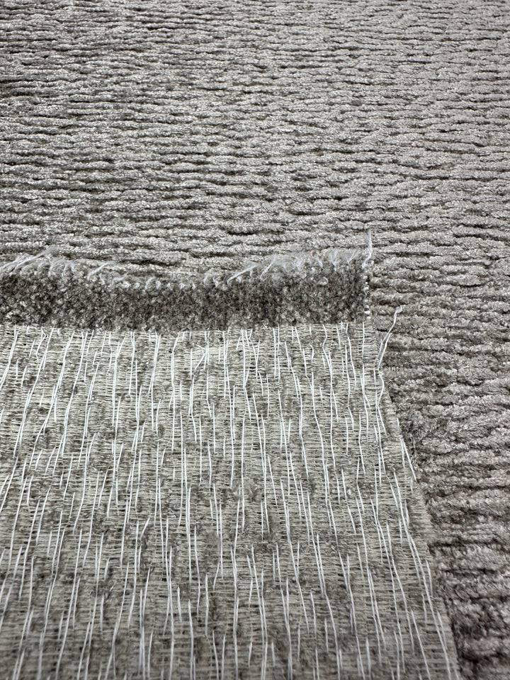 Close-up of the textured Upholstery Chenille Ezard - Silver Taupe by Super Cheap Fabrics, showcasing the velvety surface and flipped corner revealing a contrasting white thread grid pattern on the back.