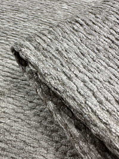 Close-up of folded Upholstery Chenille Ezard in Silver Taupe by Super Cheap Fabrics, showcasing a ribbed pattern on a matching background. The fabric has an extra heavy weight with a soft feel and distinct horizontal ridges, measuring 145cm wide.