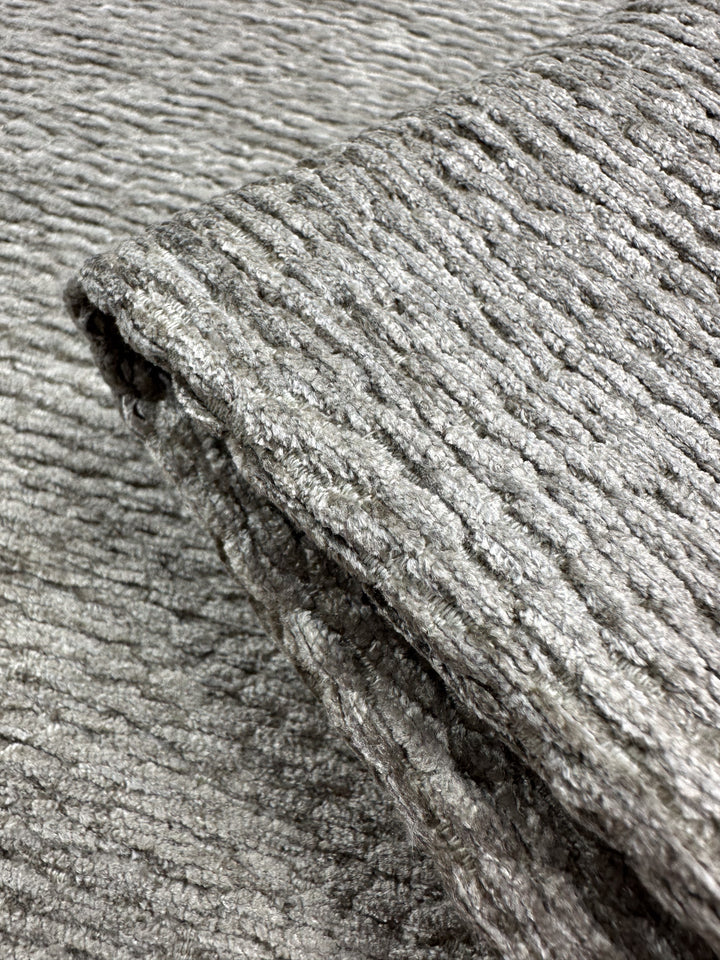 Close-up of folded Upholstery Chenille Ezard in Silver Taupe by Super Cheap Fabrics, showcasing a ribbed pattern on a matching background. The fabric has an extra heavy weight with a soft feel and distinct horizontal ridges, measuring 145cm wide.