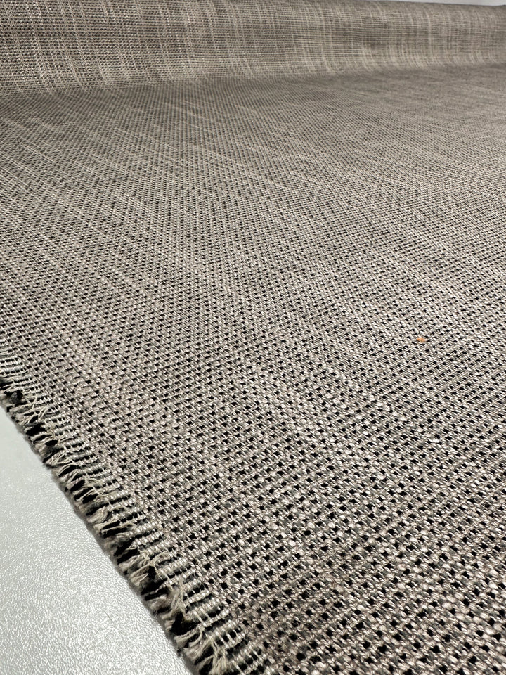 Close-up of textured open-weave Upholstery Logan - Rhino - 145cm by Super Cheap Fabrics, showcasing a grayish-brown grid pattern with small squares and slightly frayed edges on a smooth light-colored surface.
