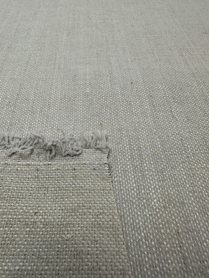 The Dresden Silver upholstery fabric from Super Cheap Fabrics showcases a light gray basket weave design with medium weight and structured texture. A fringed edge adds depth, revealing subtle pattern variations.