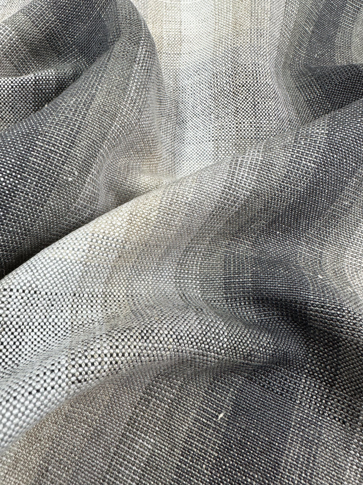 A close-up of the Super Cheap Fabrics' Pure Linen - Natural - 148cm reveals a smooth, draped luxury fabric with a gradient from light to dark gray and detailed weave, highlighting the blend of pure linen threads.