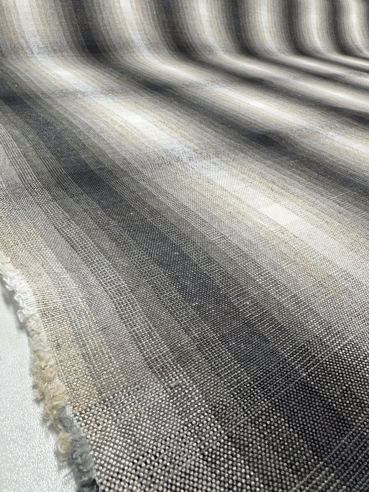 A close-up of Super Cheap Fabrics' Pure Linen - Natural - 148cm reveals a textured fabric with gray to black gradient, wavy patterns, visible woven fibers, and frayed edges at the bottom left corner, highlighting its exquisite detail.