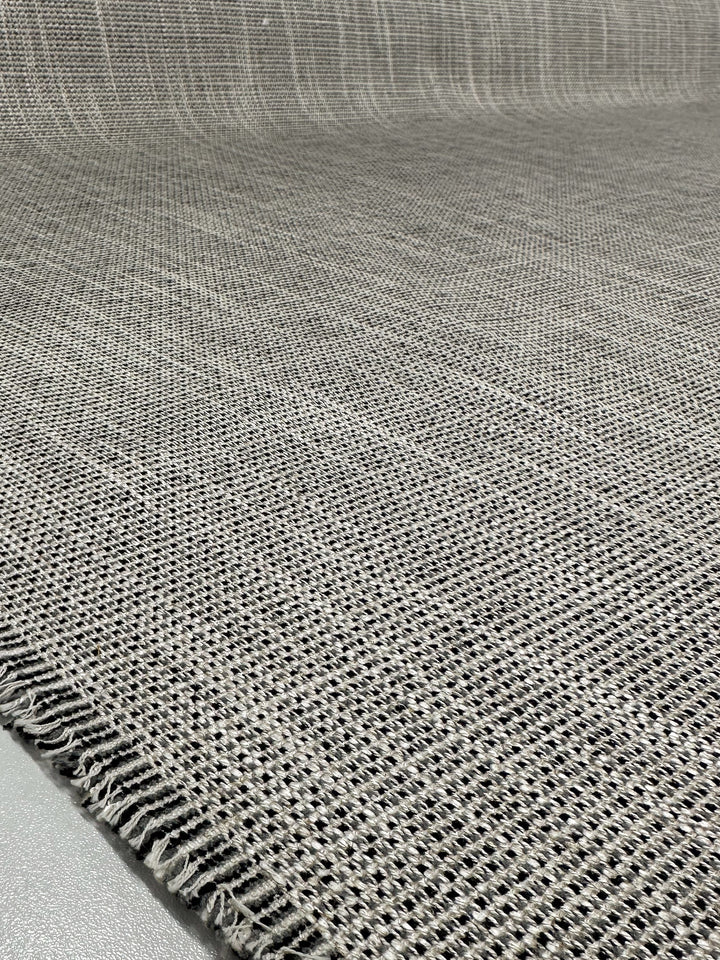 A close-up of Super Cheap Fabrics' Upholstery Logan - Salt & Pepper (145cm) in textured gray shows visible fibers and a slightly unfinished edge on a light surface. Its medium thickness and tight weave are perfect for sturdy, stylish heavy-weight upholstery projects.